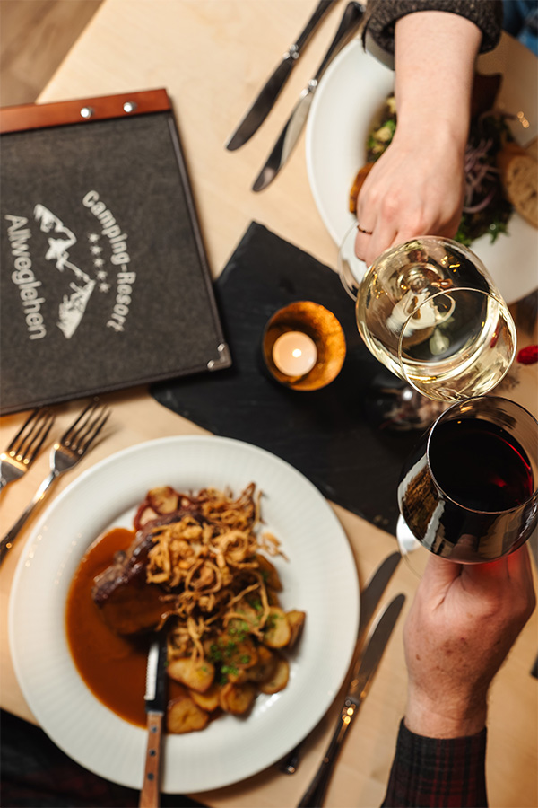 Gedeckter Tisch mit Braten, Wein und Speisekarte des Resorts
