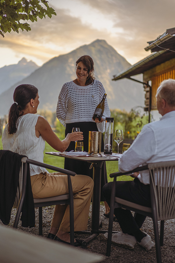 Verena Eichhorn-Lange am Tisch im Freien mit Gästen, dahinter die Allgäuer Berge