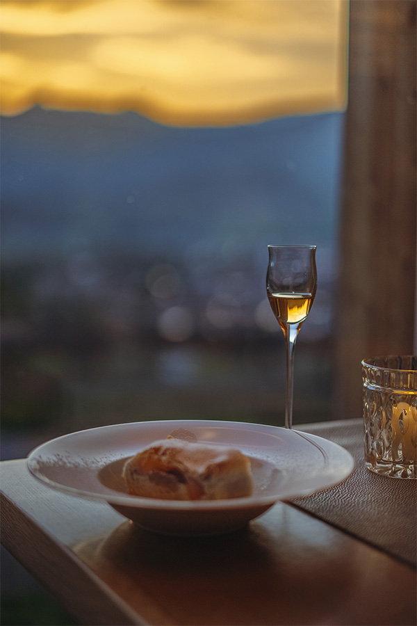 Glas Dessertwein und ein kleiner Teller auf der Brüstung, dahinter das Tal in der Dämmerung