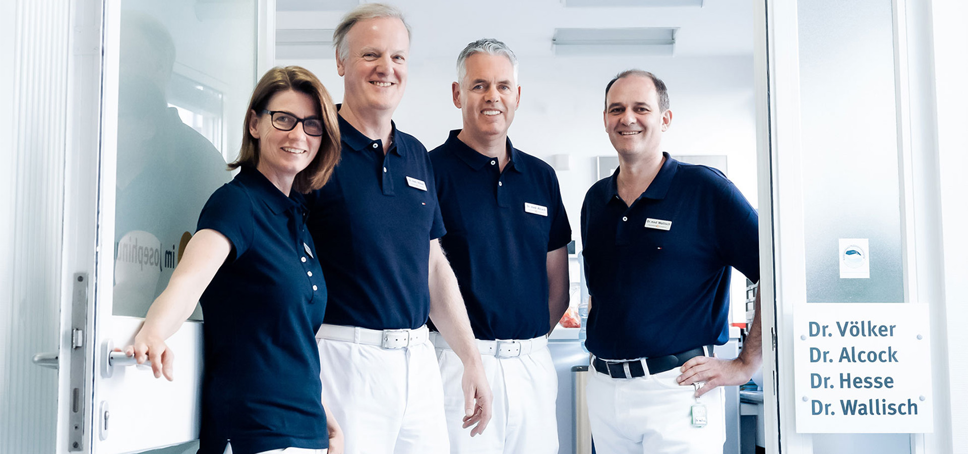 Vier Ärztinnen und Ärzte in dunkelblauen Poloshirts in einer Praxistür