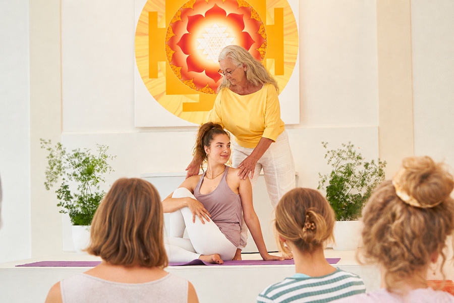 Yogalehrerin korrigiert eine Haltung, Teilnehmende schauen zu